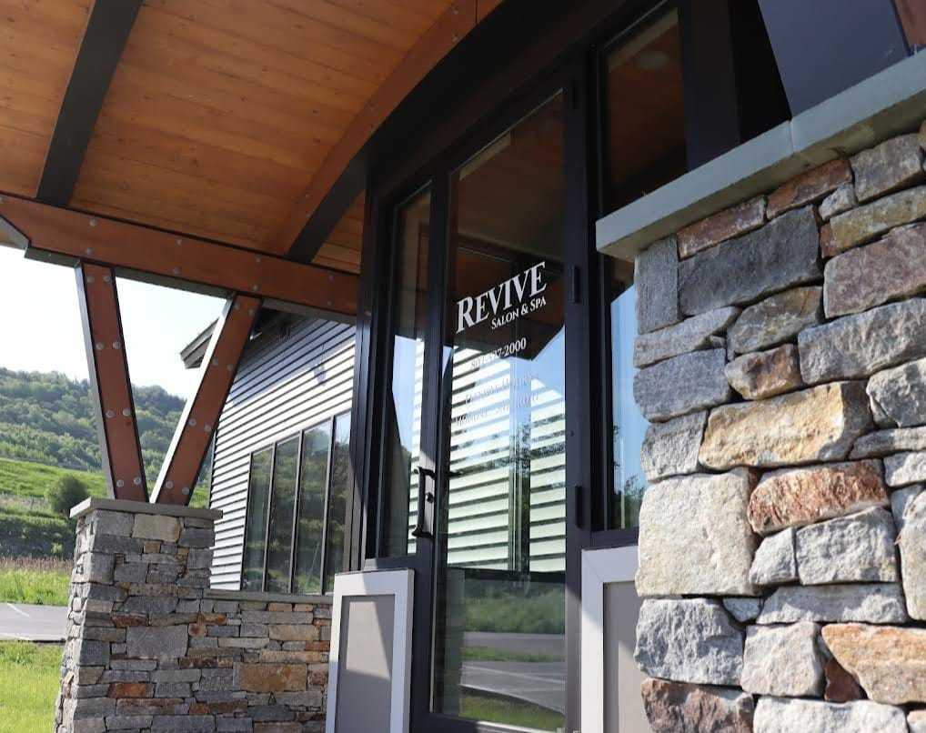 Entrance of Revive Salon & Spa with glass doors, stone pillars, and a wooden canopy.