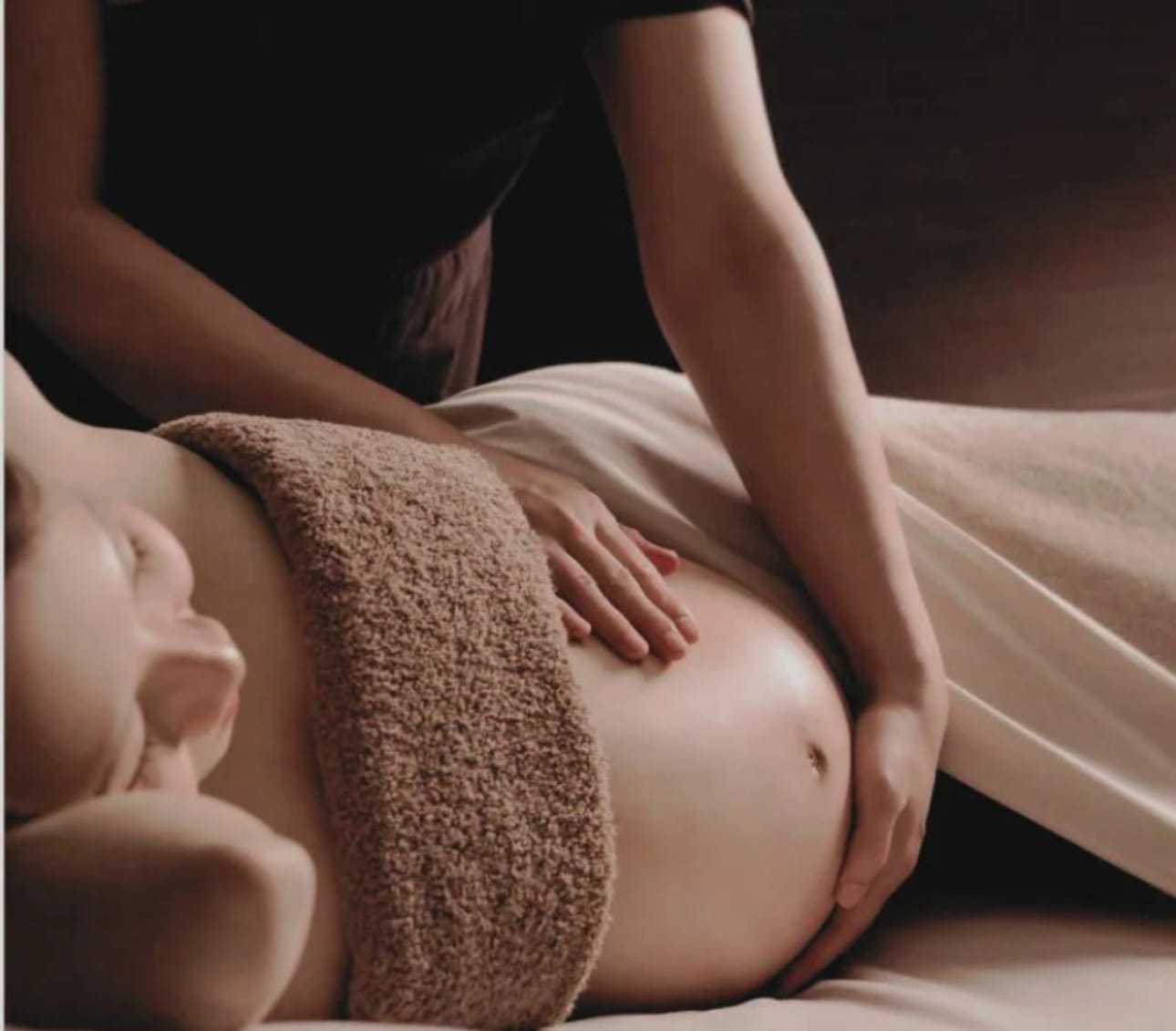 Pregnant woman receiving a gentle abdominal massage in a peaceful setting.