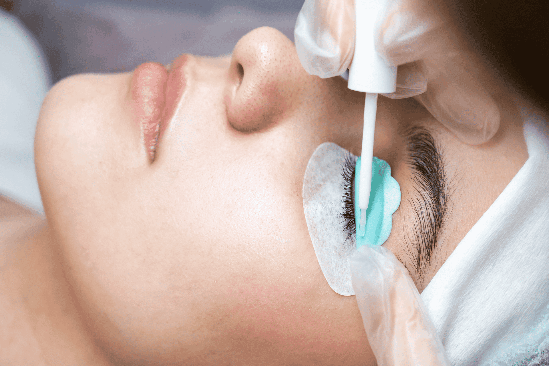 Woman receiving eyelash curling treatment, with protective pads and a professional applying solution.